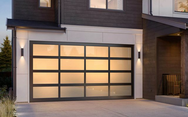 A Hörmann Luma Classic 7400 full-view glass garage door with a dark frame, lit from inside at dusk