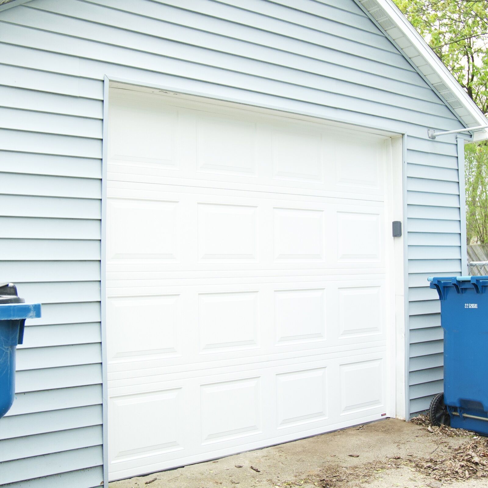 The same garage after Elevation replaced the door — a new white insulated raised-panel steel door with a photo-eye sensor on the jamb