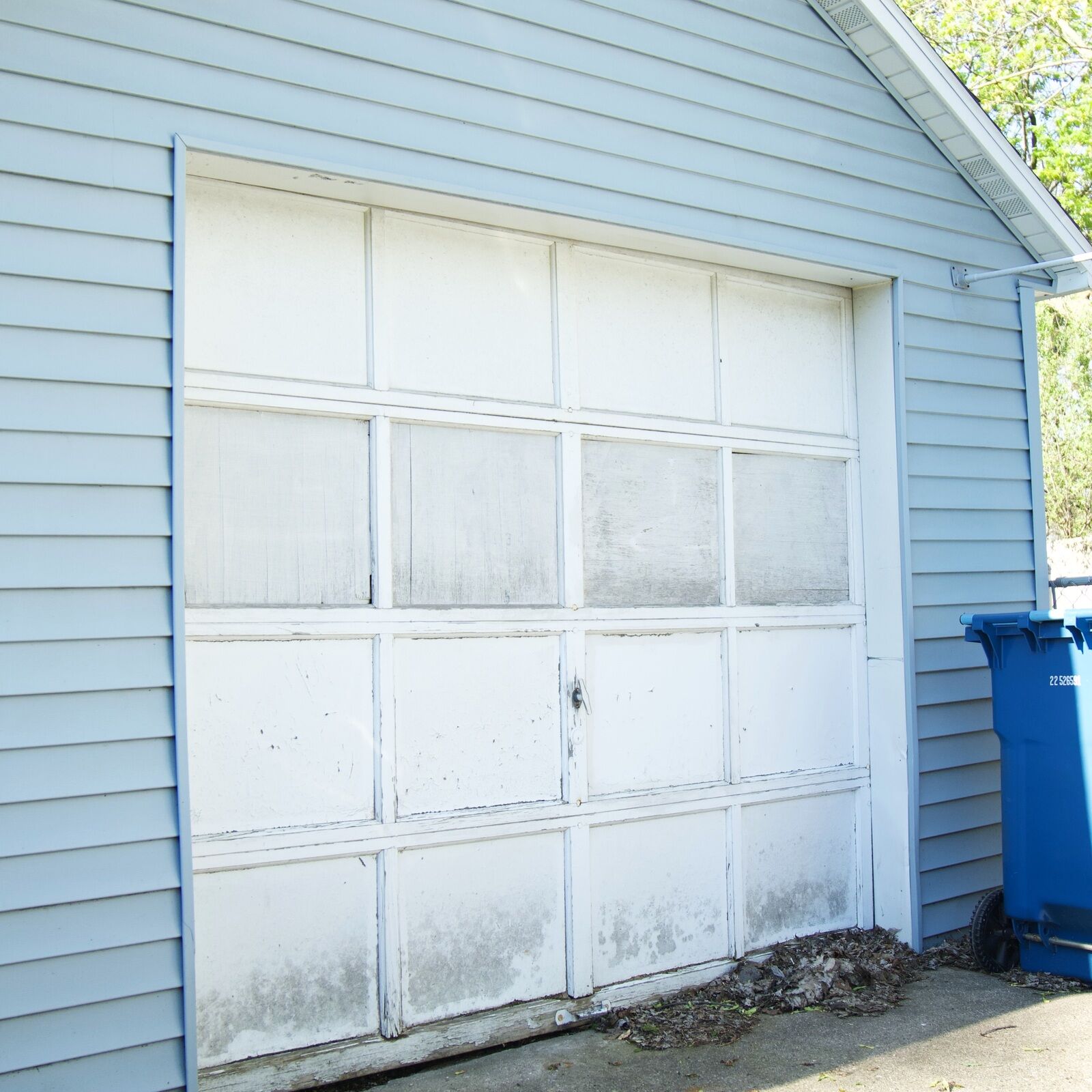 Original garage door on a Grand Rapids metro home before replacement — peeling paint, mildewed window panes and a water-damaged bottom section