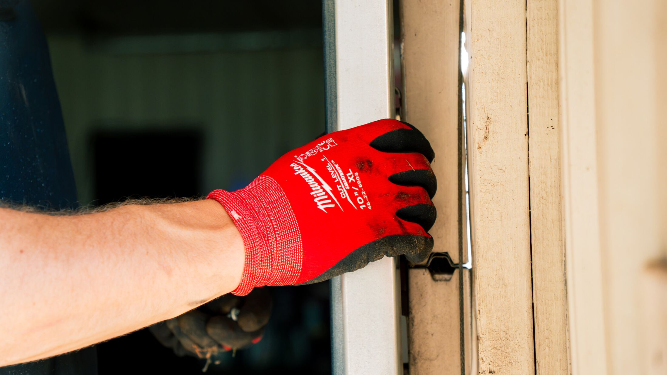 Close-up of a gloved hand at the edge of a garage door where the panel meets the jamb and weather seal