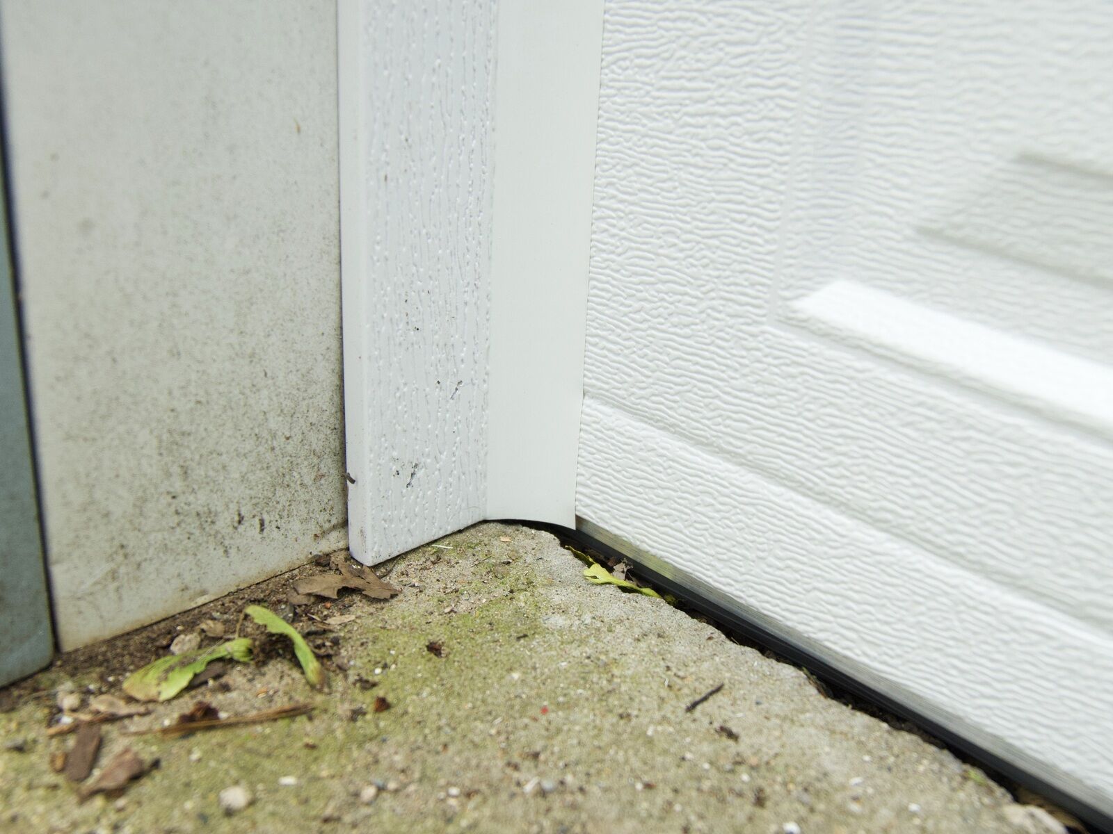 The bottom corner of a garage door showing the side jamb, weather seal, and concrete floor