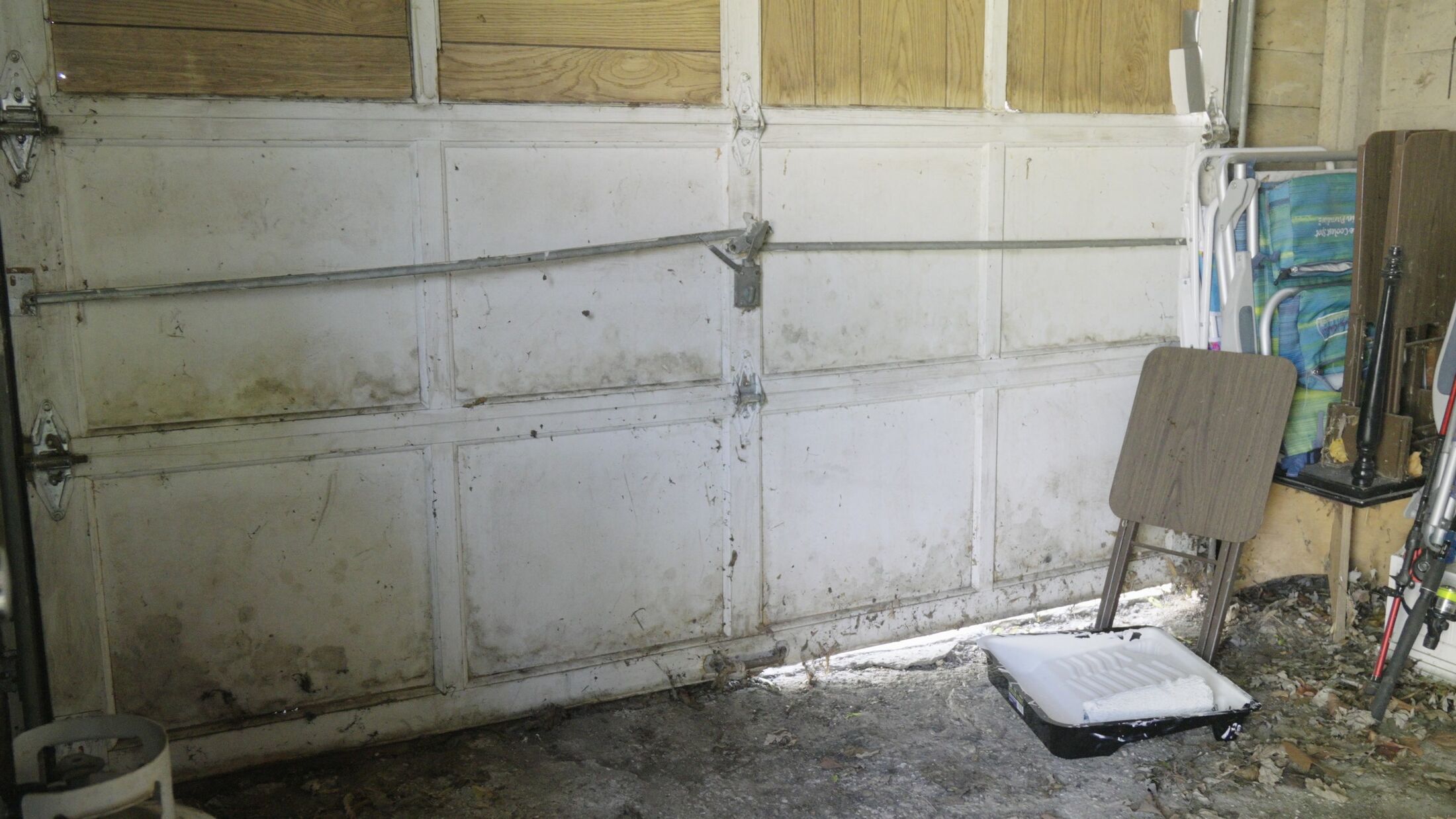 Inside the old garage door before removal — rusted struts, filthy panels and a rotted bottom rail