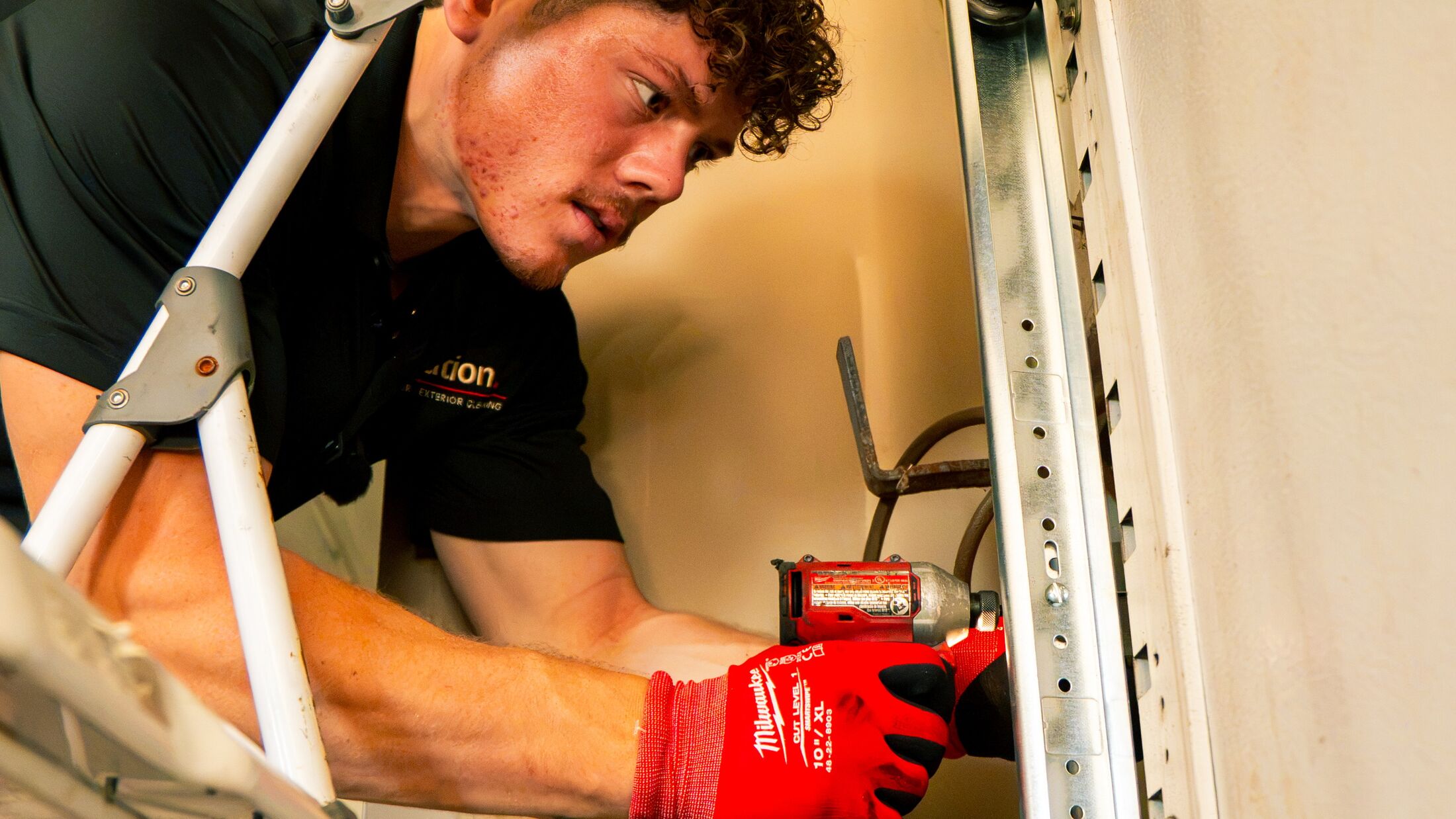 An Elevation technician on a ladder fastening the opener rail at the top of a garage door