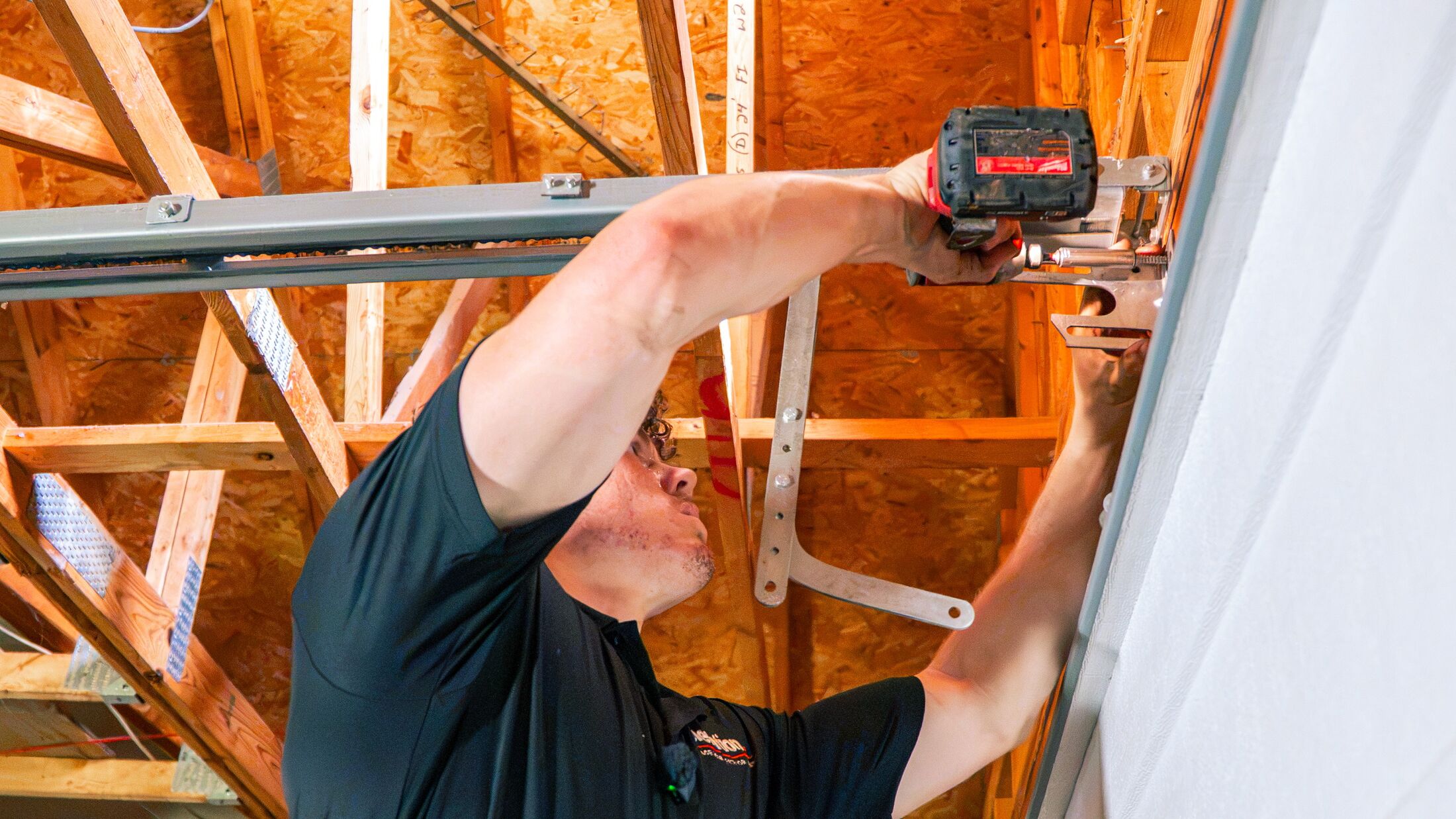 An Elevation technician fastening the horizontal track of a garage door overhead with an impact driver